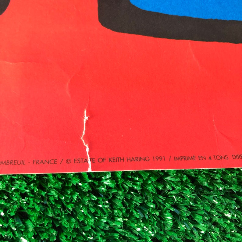 May include: An abstract art print in red, blue and black with the text "ESTATE OF KEITH HARING 1991 / IMPRIM&Eacute; EN 4 TONS DIRECTES / OMBREUIL - FRANCE" at the bottom.