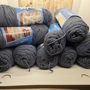 May include: A stack of blue yarn balls, some with labels that say "Soyelle" and "Soft and Cozy Yarn from Sayelle".
