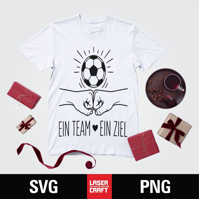May include: White t-shirt with a black graphic of a soccer ball above two fists bumping. The text "EIN TEAM EIN ZIEL" is below the graphic. The image includes wrapped gifts and a dark plate with a drink.