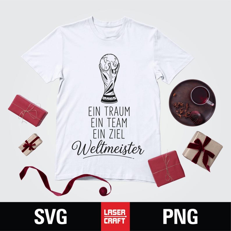May include: White t-shirt with a black graphic of a trophy and the text "EIN TRAUM EIN TEAM EIN ZIEL Weltmeister". The shirt is surrounded by wrapped gifts and a decorative plate.