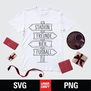 May include: White t-shirt with a black graphic of a wooden signpost pointing to "Stadion", "Freunde", "Bier", and "Fu&szlig;ball". The image includes wrapped gifts and a dark plate with a drink.