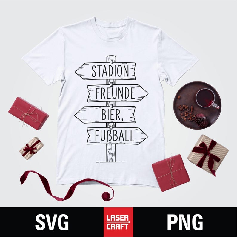 May include: White t-shirt with a black graphic of a wooden signpost pointing to "Stadion", "Freunde", "Bier", and "Fu&szlig;ball". The image includes wrapped gifts and a dark plate with a drink.