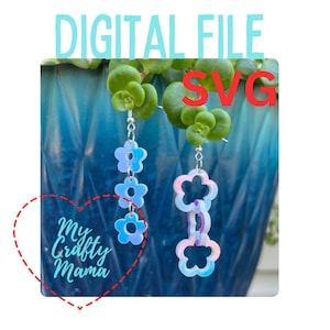 May include: A pair of iridescent blue flower-shaped earrings with a silver chain. The earrings are hanging from a plant in a blue planter. The text "My Crafty Mama" is in a red heart shape.