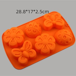 Könnte beinhalten: Orangefarbene Silikon-Backform mit sechs Vertiefungen in Form eines Schmetterlings, Marienkäfers und einer Blume. Die Form misst 28,8 x 17 x 2,5 Zentimeter.