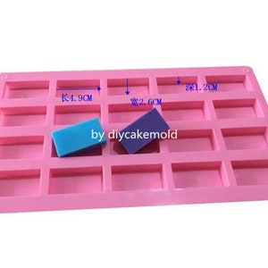 以下が含まれることがあります： ピンクのシリコンモールドで、長方形のくぼみが18個あります。モールドの長さは4.9cm、幅は2.6cmです。青い石鹸と紫色の石鹸が2つモールドに入っています。