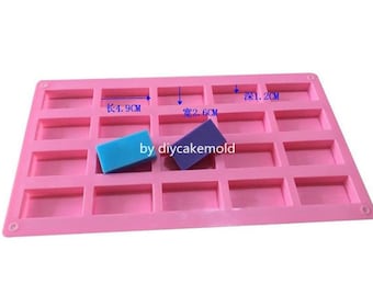 Puede incluir: Molde de silicona rosa con 18 cavidades rectangulares. El molde mide 4,9 cm de largo y 2,6 cm de ancho. Dos barras de jabón azules y moradas están en el molde.