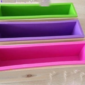 May include: Three silicone soap molds in a wooden box. The molds are green, purple, and pink. The box is made of natural wood.