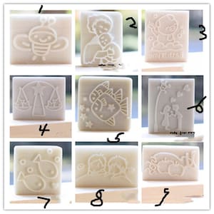 May include: Set of 9 white soap stamps with various designs, including a bee, a couple, a fish, a scale, a pig, and a heart. The stamps are numbered 1 through 9.