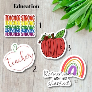 May include: A collection of teacher-themed stickers. One sticker reads "Teacher Strong" in rainbow colors. Another features a red apple with the word "Teacher." A third sticker shows a rainbow with the text "Remember why you started."
