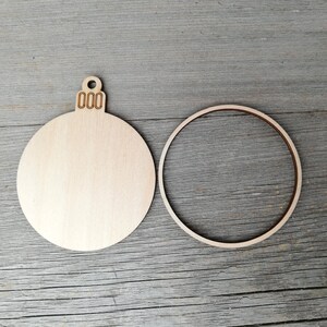 May include: A wooden Christmas bauble with a blank circle and a separate circle for the back. The bauble has a small loop at the top and the text "000" is engraved on the loop.