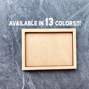 May include: A rectangular light-colored wooden frame with a smooth finish and a recessed center panel. The text "AVAILABLE IN 13 COLORS!!!" is printed in white capital letters above the wooden frame.
