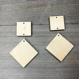 Op de afbeelding: Vier onafgewerkte houten vormen, twee vierkanten en twee ruiten, met gaten geboord in de bovenkant om op te hangen. De vormen zijn gerangschikt op een houten achtergrond.