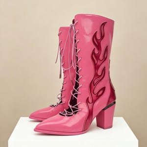 May include: A pair of bright pink patent leather mid-calf boots featuring a pointed toe, a block heel, and a lace-up front closure. The side of each boot is decorated with a dark red flame-shaped appliqué that extends from the heel to the shaft.
