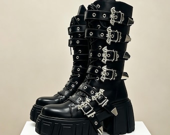May include: Black knee-high boots with multiple silver buckles and straps. The boots have a chunky platform sole and a rounded toe. The boots are made of a smooth, shiny material and have a gothic or punk aesthetic.