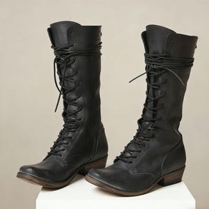 May include: A pair of black mid-calf boots featuring a lace-up front design with long black laces that wrap around the top of the shaft. The boots have a rounded toe, a low stacked wooden heel, and a side zipper closure for easy access and fit.