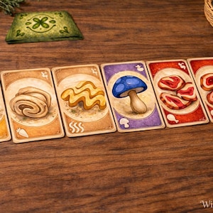 Peut inclure: Jeu de cartes illustrées avec des aliments comme une carotte, un champignon et de la viande. Les cartes ont une esthétique vintage sur un fond en bois. Une carte verte avec un motif de trèfle est également présente.