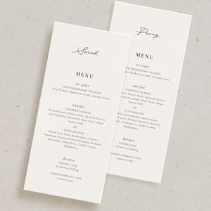 May include: Two white menu cards with elegant script names at the top. The menus list dishes like Charred Salmon and Filet Mignon. The cards are on a light gray surface, ideal for weddings or special events.