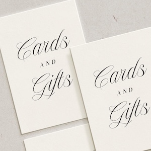 Könnte beinhalten: Drei rechteckige Karten mit den Worten "Cards and Gifts" in eleganter schwarzer Schrift. Die Karten haben eine cremefarbene Farbe und sind auf einer hellgrauen Oberfläche angeordnet.