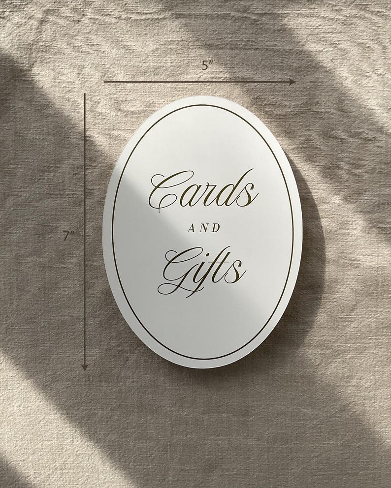 May include: An oval, white sign that is 7 inches tall and 5 inches wide, with the words "Cards AND Gifts" in elegant script. The sign has a thin, dark border.