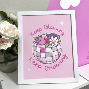 May include: Pink framed print with a white disco ball with flowers on top. The text reads "Keep Glowing Keep Growing".