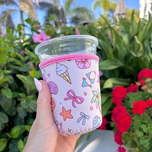 May include: A pink neoprene cup holder with a fun summer design featuring ice cream cones, seashells, palm trees, bows, and swimsuits.