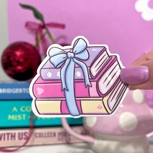 May include: A stack of four pink and purple books with a blue bow on top. The books are decorated with white flowers and hearts.