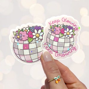 May include: Two pink and white glitter stickers with a disco ball design and flowers. The text on the stickers reads "Keep Glowing Keep Growing".