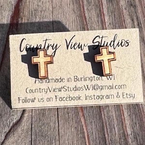 May include: Two wooden cross earrings on a card with the text "Country View Studios." The earrings are light brown with a darker brown outline. The card also includes the text "Handmade in Burlington, WI."