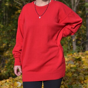May include: A red long-sleeved sweater with a round neckline. The sweater is made of a soft, comfortable material and has a relaxed fit.