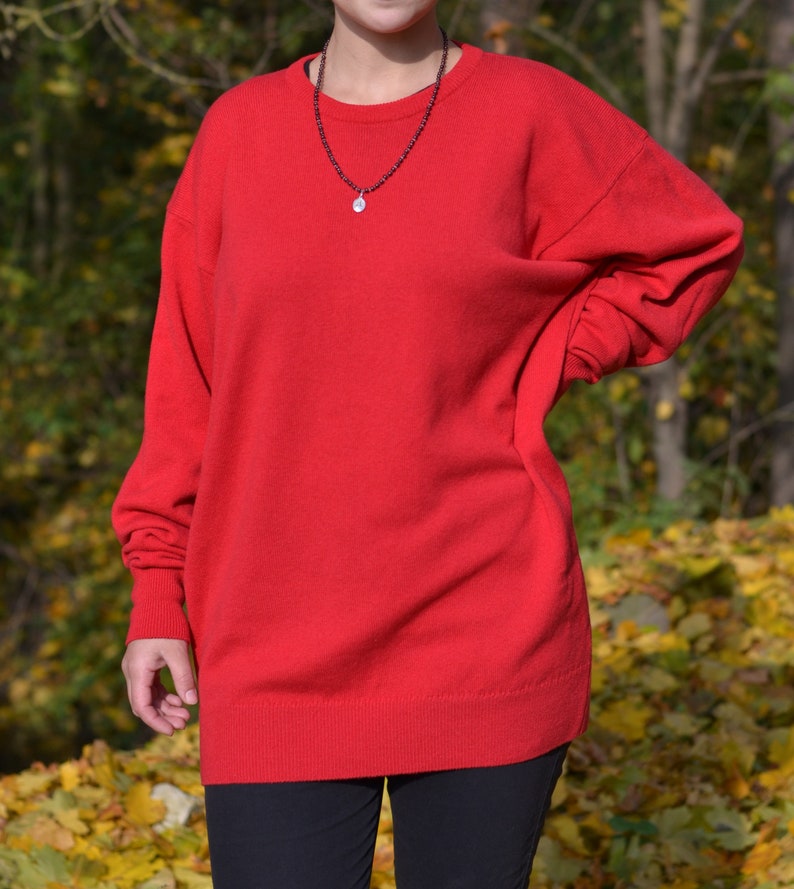 May include: A red long-sleeved sweater with a round neckline. The sweater is made of a soft, comfortable material and has a relaxed fit.