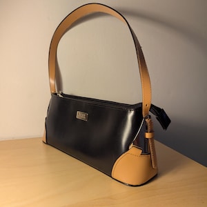 May include: A black leather handbag with a tan leather trim and a top handle. The bag has a silver zipper and a silver logo that says "DKNY".