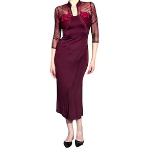 Op de afbeelding: Een bordeauxrode jurk met een bijpassende doorschijnende bolero met lange mouwen. De bolero heeft een hoge kraag en bloemaccenten op de borst. De jurk is midi-lang en heeft een eenvoudig, elegant ontwerp.