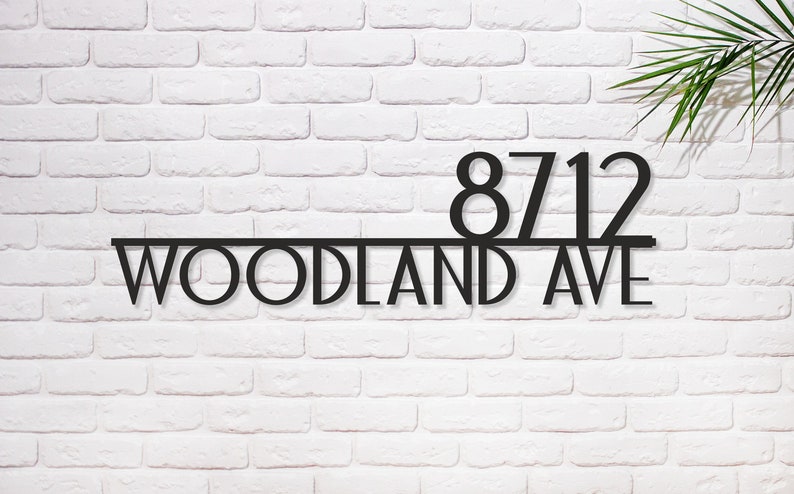May include: Black metal house number sign with the numbers 8712 and the text "WOODLAND AVE" on a white brick wall.