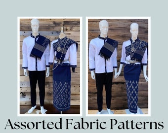 May include: Two mannequins wearing traditional Thai clothing. The clothing is white with blue and gold patterned fabric. The mannequins are standing in front of a wooden wall.