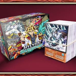 May include: A trading card deck box featuring an illustration of Sylvio Sawatari and various characters, accompanied by a stack of trading cards secured with a rubber band. The top card displays a white armored figure with the numbers 2400 and 1000.