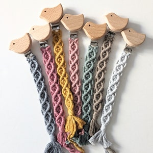 Peut inclure: Sept hochet en macramé coloré pour bébé avec des pinces en bois en forme d'oiseau. Les hochets sont faits de différentes couleurs, dont le rose, le bleu, le jaune et le gris.