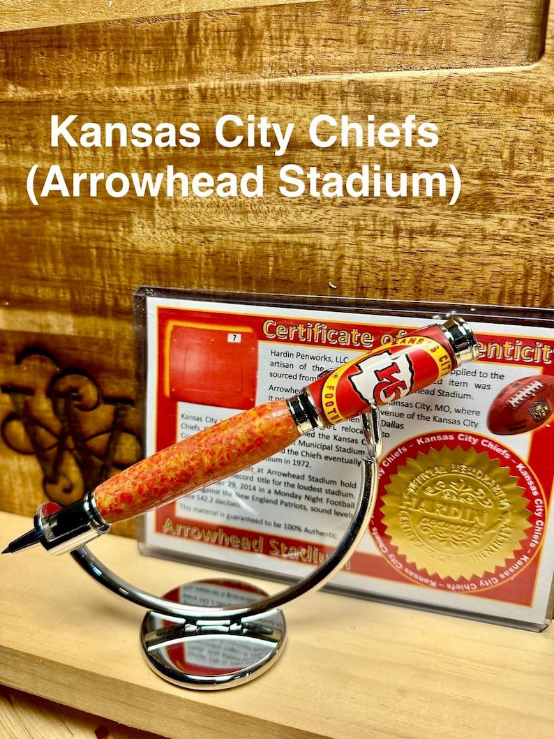 May include: A red, white, and gold pen with a Kansas City Chiefs logo and the words "Arrowhead Stadium" on the barrel. The pen is on a silver stand and has a certificate of authenticity.