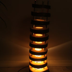 May include: A tall, wooden floor lamp with a stack of circular wood slices. Each slice has a light bulb in the center, creating a warm glow. The lamp is on a wooden floor.