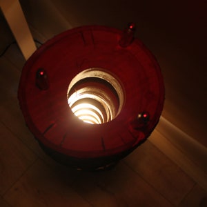 May include: A red lamp with a spiral design inside, casting a warm glow. The lamp has a circular base with three small holes.