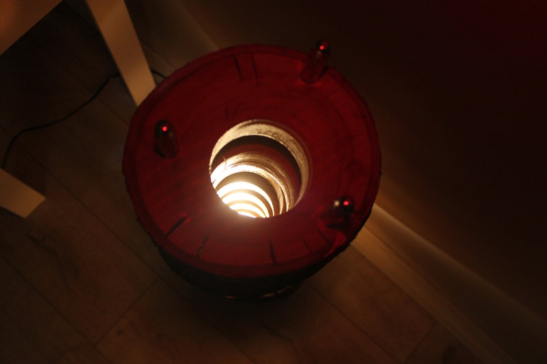 May include: A red lamp with a spiral design inside, casting a warm glow. The lamp has a circular base with three small holes.