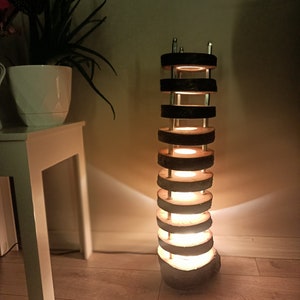 May include: A tall, modern floor lamp made from stacked wood slices. The lamp has a warm, inviting glow and is a unique and stylish addition to any home.