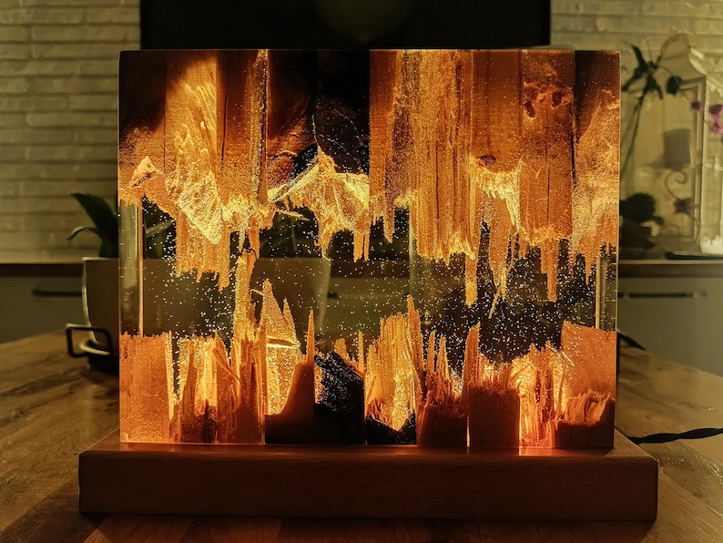 The Fission Resin Lamp, an Epoxy Resin Nightlamp with Oak Wood & Resin Decor, is a Wooden Modern Table Lamp ideal for home decor. This Resin Nightstand Lamp combines natural oak and epoxy resin, offering a sleek, contemporary glow for your nightstand or living space in a unique, handcrafted design.