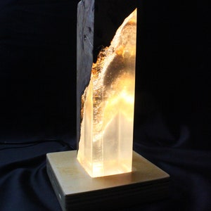 May include: A wooden lamp base with a clear resin insert, lit from within, creating a warm glow. The resin has a natural wood grain pattern.