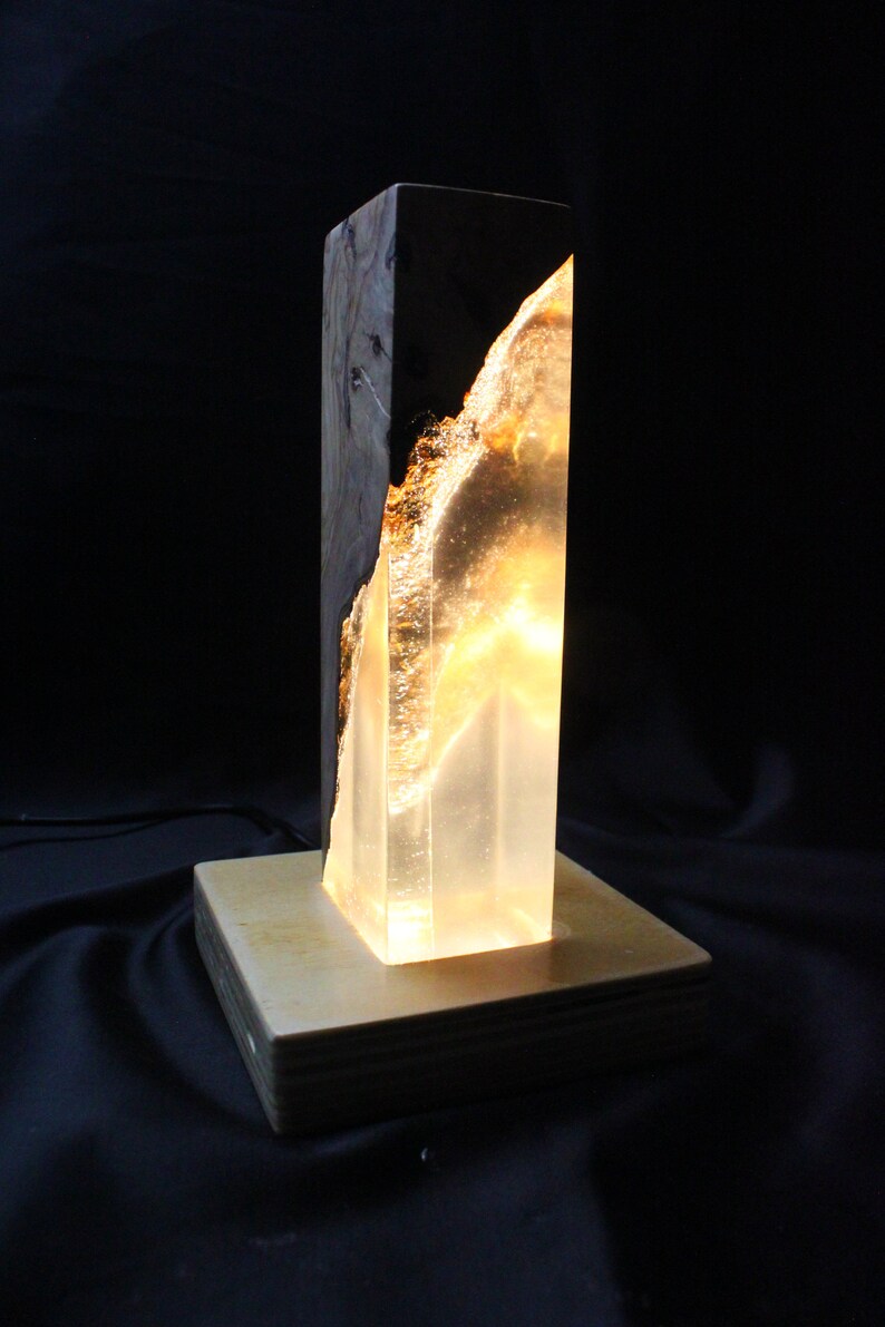 May include: A wooden lamp base with a clear resin insert, lit from within, creating a warm glow. The resin has a natural wood grain pattern.