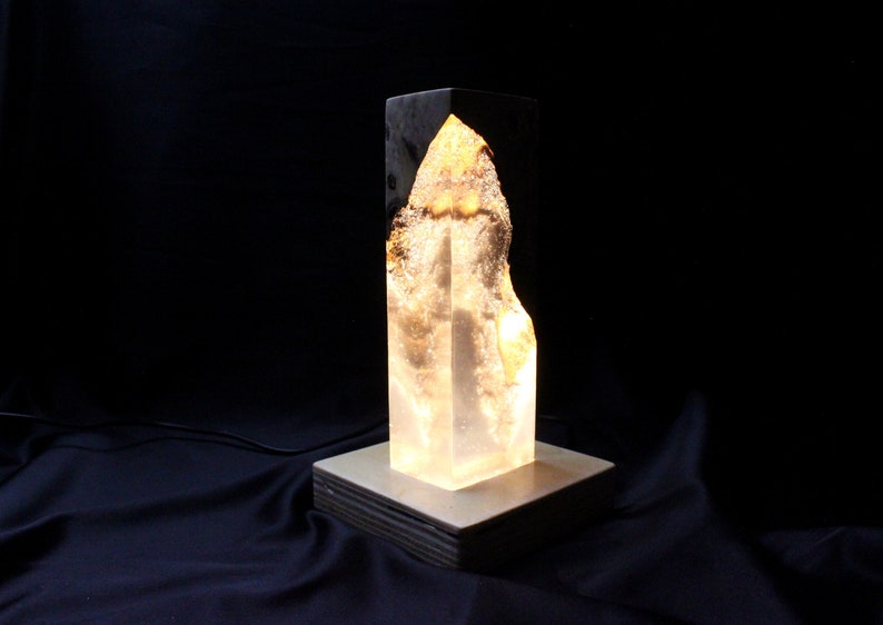May include: A clear glass lamp with a white base and a golden interior. The lamp is lit and casts a warm glow.
