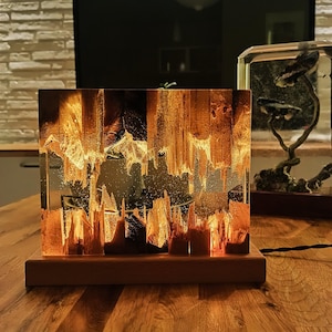 The Fission Resin Lamp, an Epoxy Resin Nightlamp with Oak Wood & Resin Decor, is a Wooden Modern Table Lamp ideal for home decor. This Resin Nightstand Lamp combines natural oak and epoxy resin, offering a sleek, contemporary glow for your nightstand or living space in a unique, handcrafted design.
