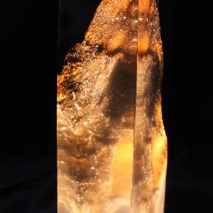 May include: A tall, clear glass sculpture with a golden, swirling pattern inside. The sculpture is lit from within, creating a warm glow.