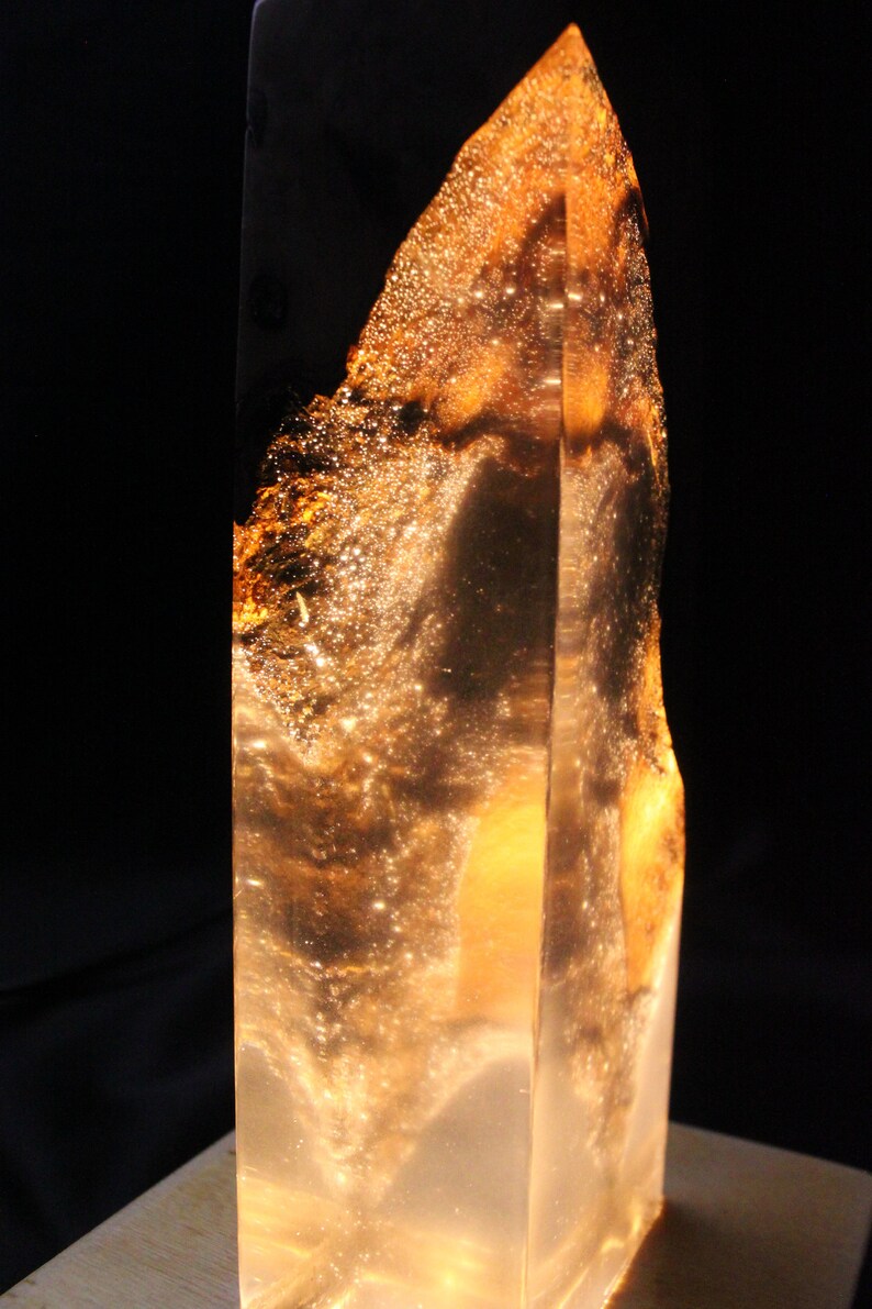 May include: A tall, clear glass sculpture with a golden, swirling pattern inside. The sculpture is lit from within, creating a warm glow.