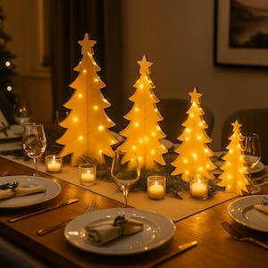 Könnte beinhalten: Eine festliche Tischdekoration mit vier beleuchteten Weihnachtsbaumdekorationen aus Holz. Jeder Baum ist unterschiedlich groß und hat einen Stern an der Spitze. Der Tisch ist mit Tellern, Besteck und Kerzen gedeckt.
