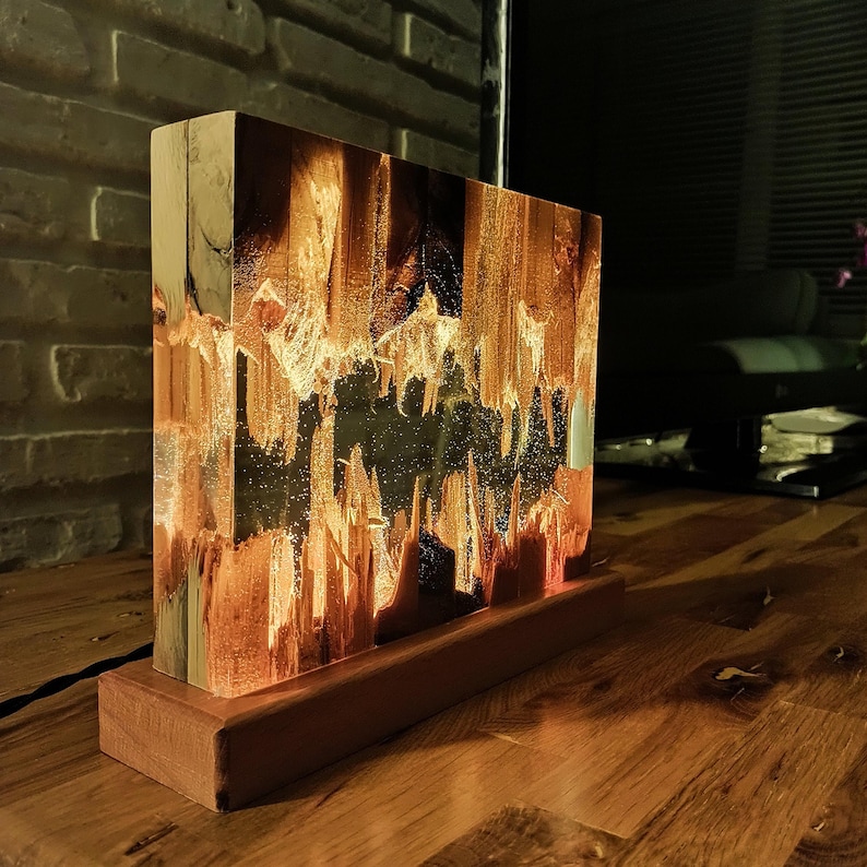 The Fission Resin Lamp, an Epoxy Resin Nightlamp with Oak Wood & Resin Decor, is a Wooden Modern Table Lamp ideal for home decor. This Resin Nightstand Lamp combines natural oak and epoxy resin, offering a sleek, contemporary glow for your nightstand or living space in a unique, handcrafted design.